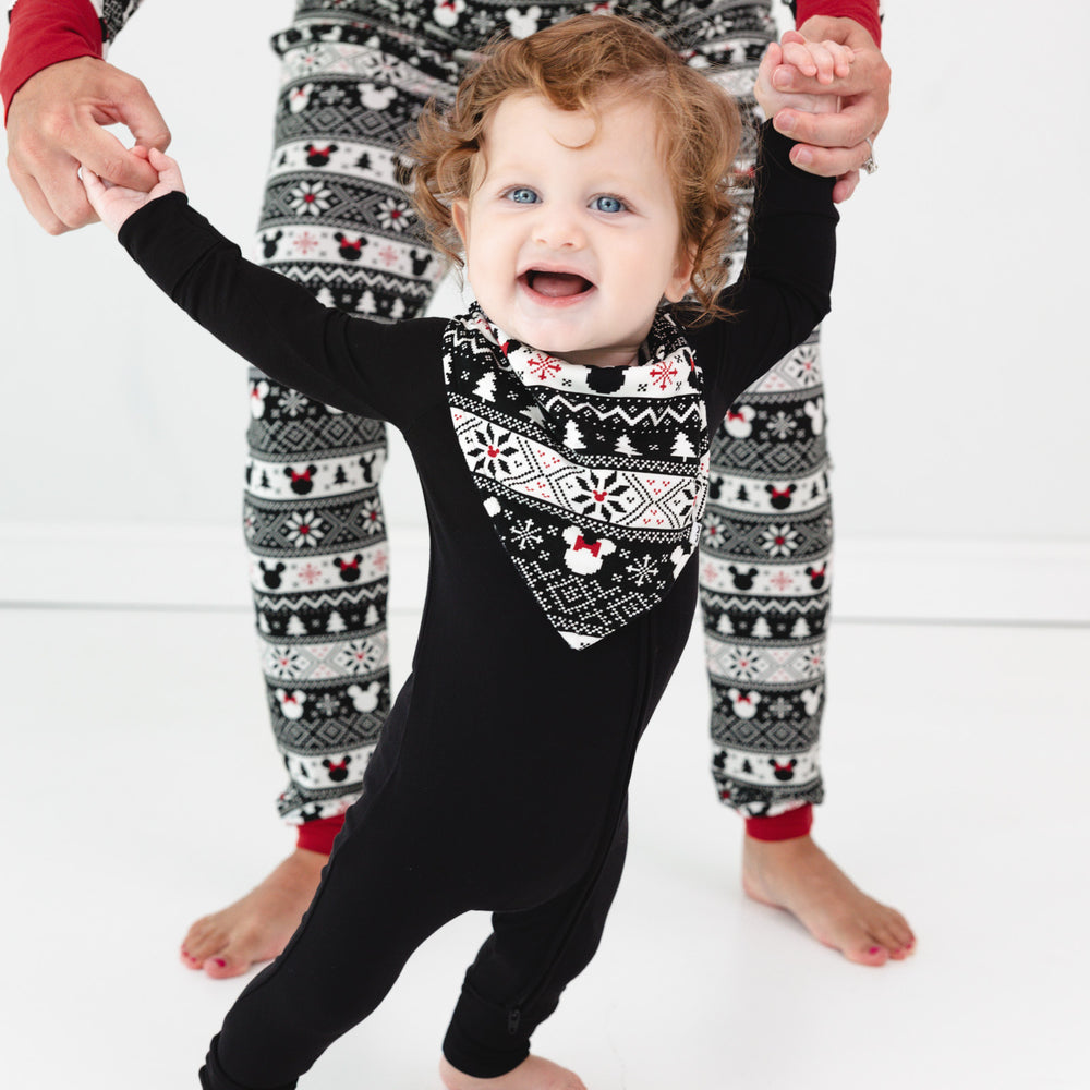 Child held up by their parent wearing Mickey Fair Isle bandana bib and black zippy. Parent is wearing Mickey Fair Isle pjs in adult styles