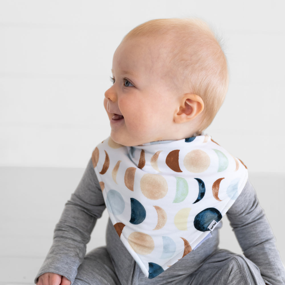 Close up of a child wearing a Luna Neutral bandana bib over a heather gray zippy