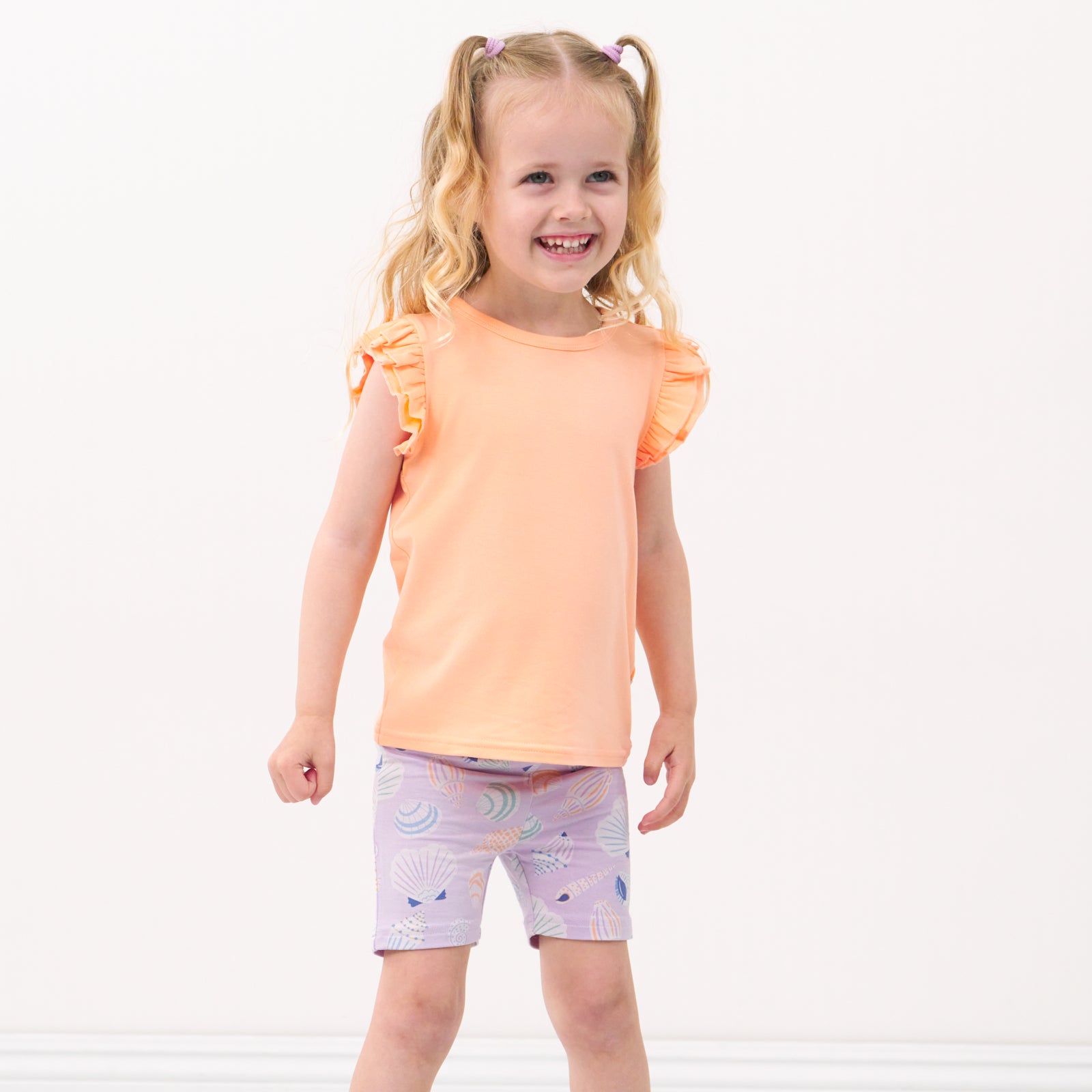 Child wearing Sandy Treasures bike shorts paired with Peach Nectar flutter tee