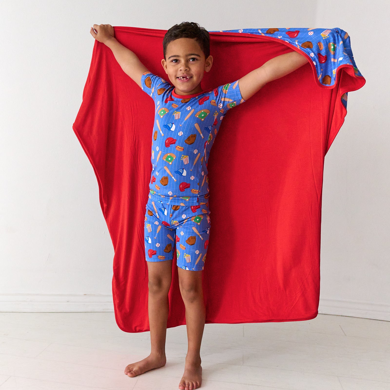 Child wearing a Blue All Stars printed large cloud blanket over his shoulders matching his two piece short sleeves and shorts pajama set