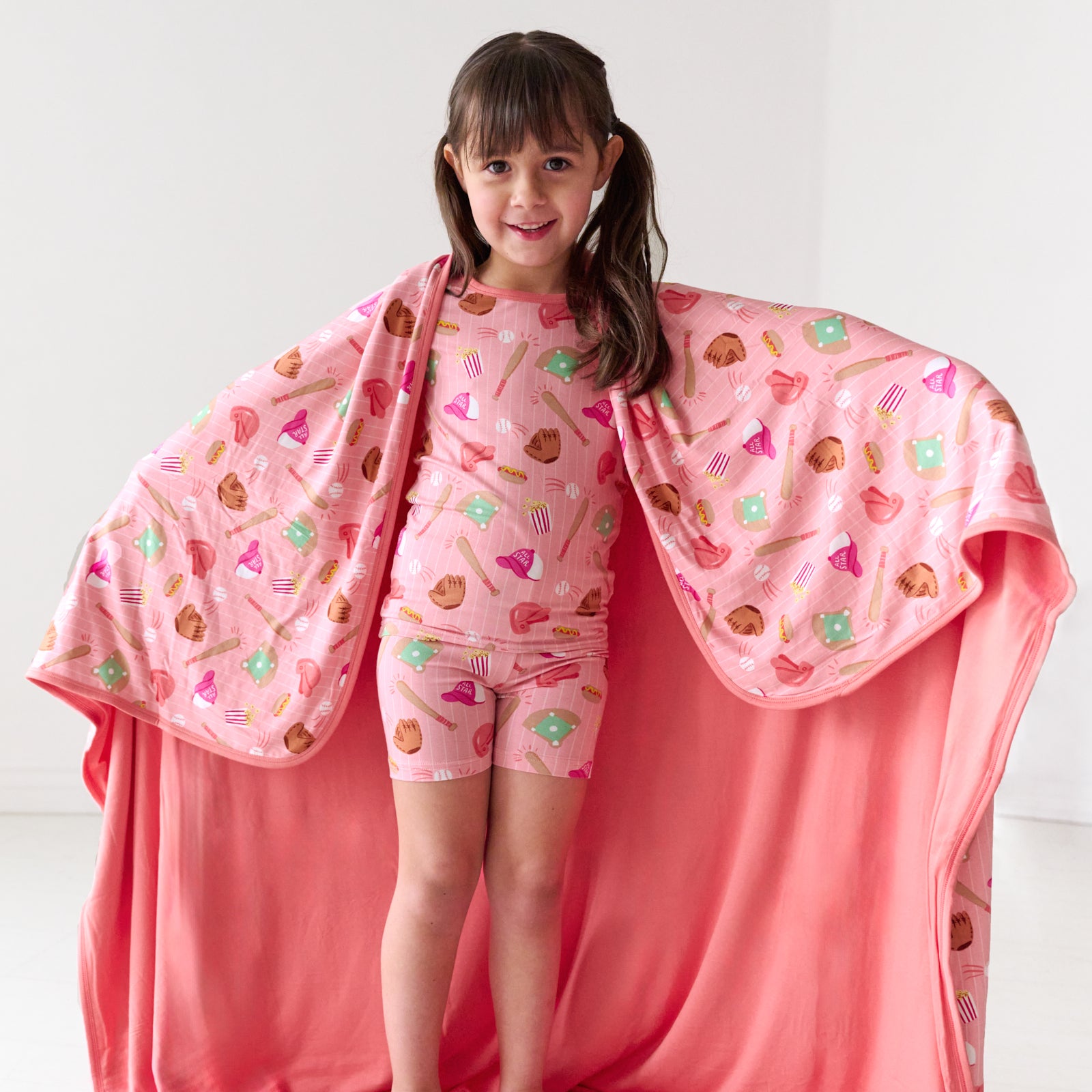 Child wearing a Pink All Stars printed large cloud blanket over her shoulders matching her two piece short sleeves and shorts pajama set