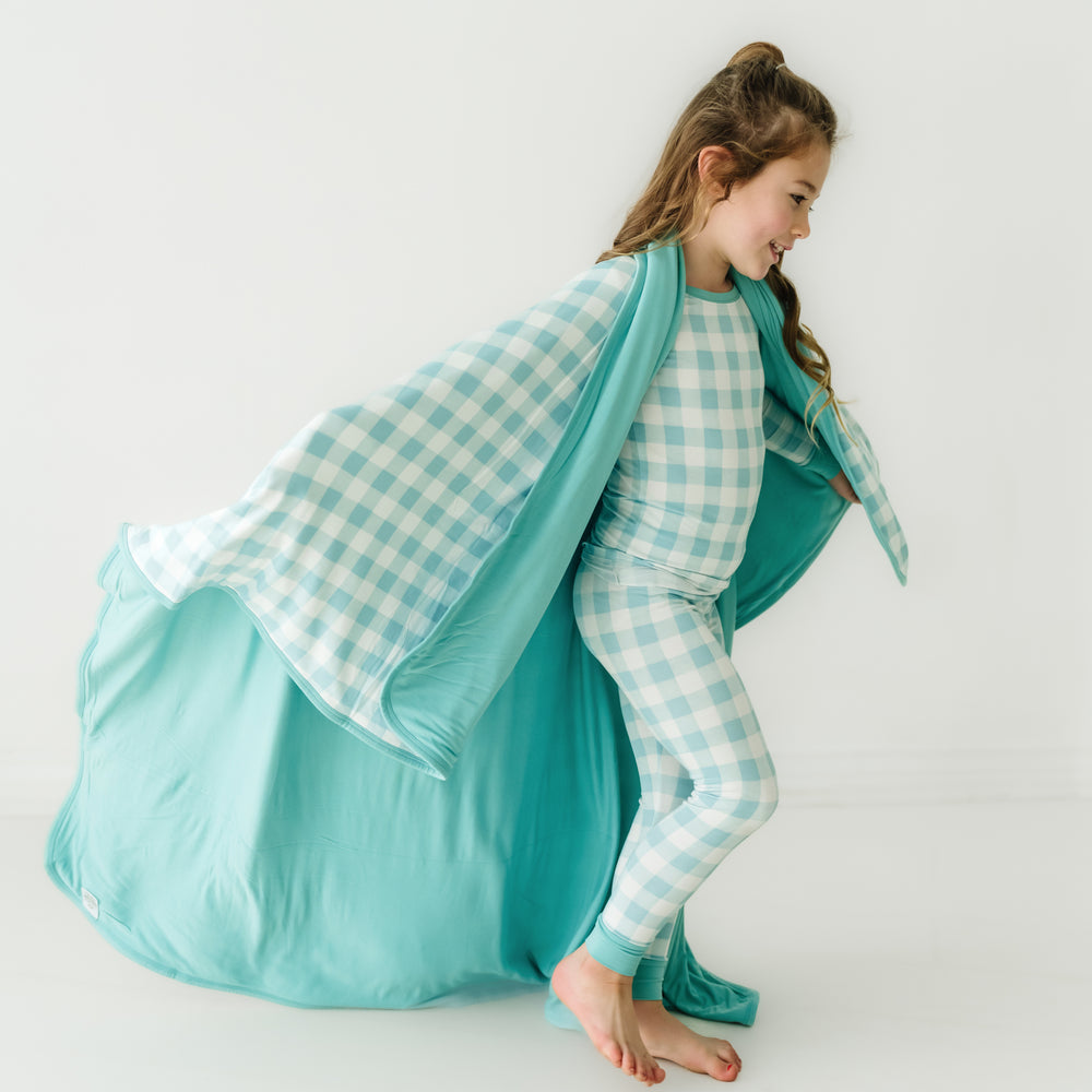 Click to see full screen - Child playing wearing a Aqua Gingham cloud blanket over her shoulders and a matching aqua gingham two piece pajama set