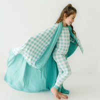 Child playing wearing a Aqua Gingham cloud blanket over her shoulders and a matching aqua gingham two piece pajama set