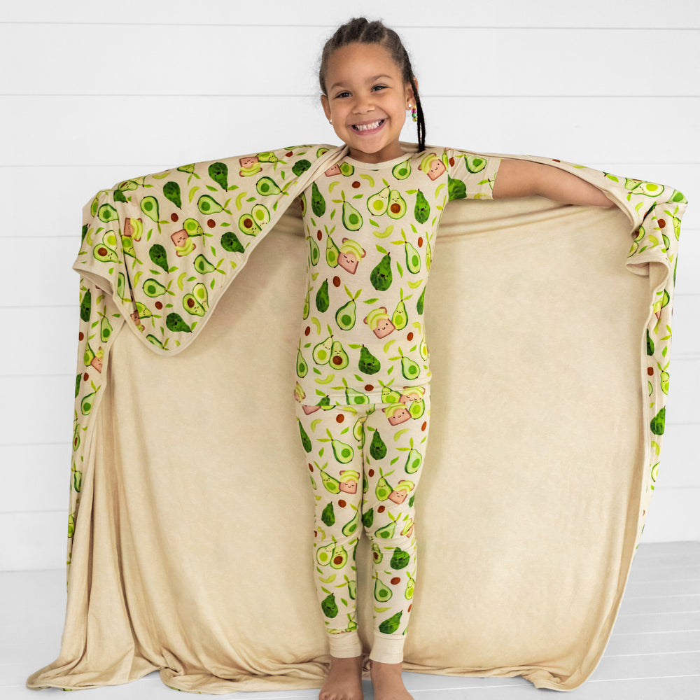 child holding out an Avocado Toast cloud blanket wearing a matching two piece pjs set