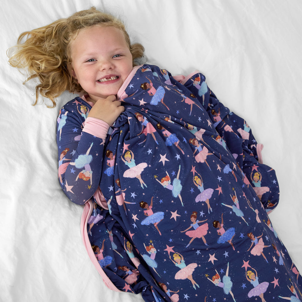 Child laying on a bed tucked under a Twilight Ballet cloud blanket