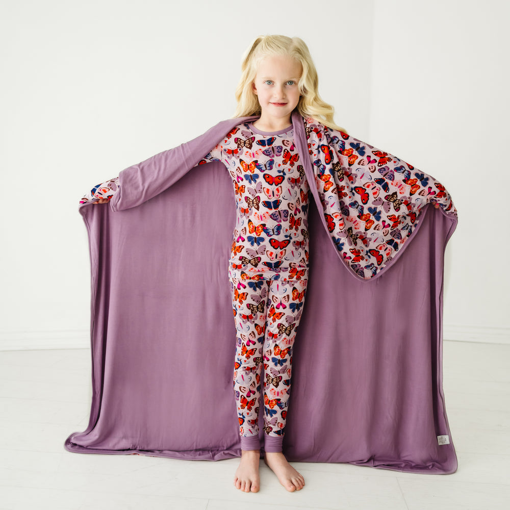 Child holding out a Butterfly Kisses large cloud blanket behind them, detailing the solid purple backing, and wearing matching pajamas