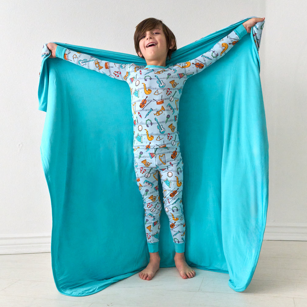 Child holding out a Play Along large cloud blanket behind them detailing the solid backing and wearing matching pajamas