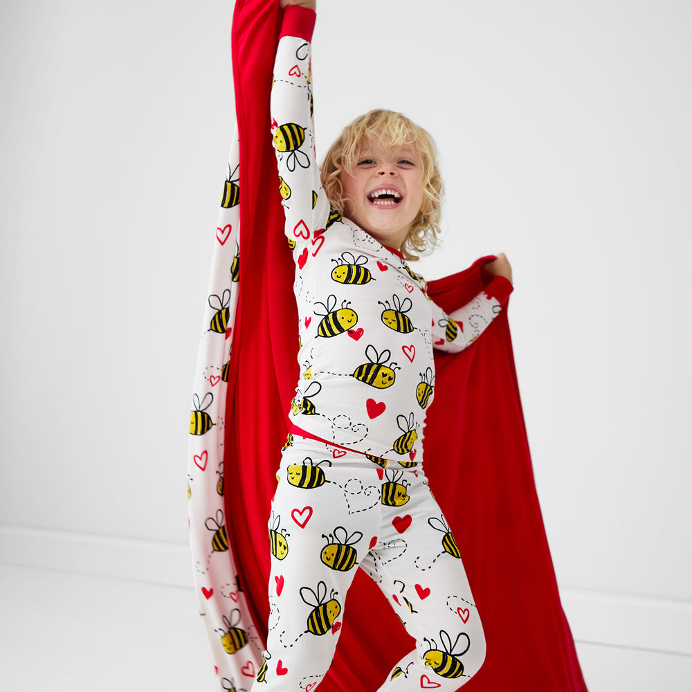 Image of a child holding up a Bee Mine blanket and wearing a matching printed two piece pj set