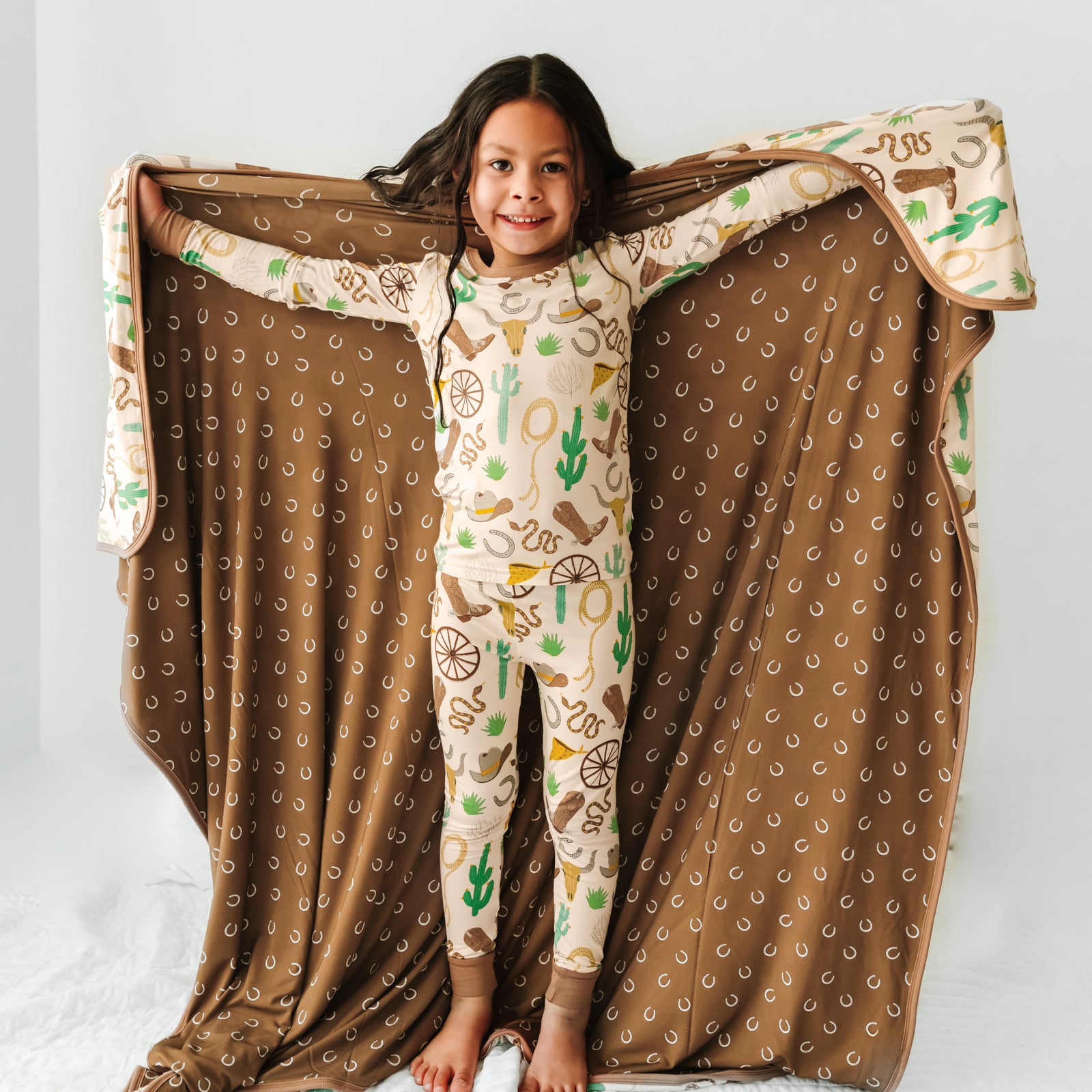 Child holding up in a Caramel Ready to Rodeo large cloud blanket wearing a matching printed pajama set