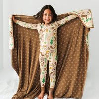 Child holding up a Caramel Ready to Rodeo blanket wearing a matching printed two piece pajama set