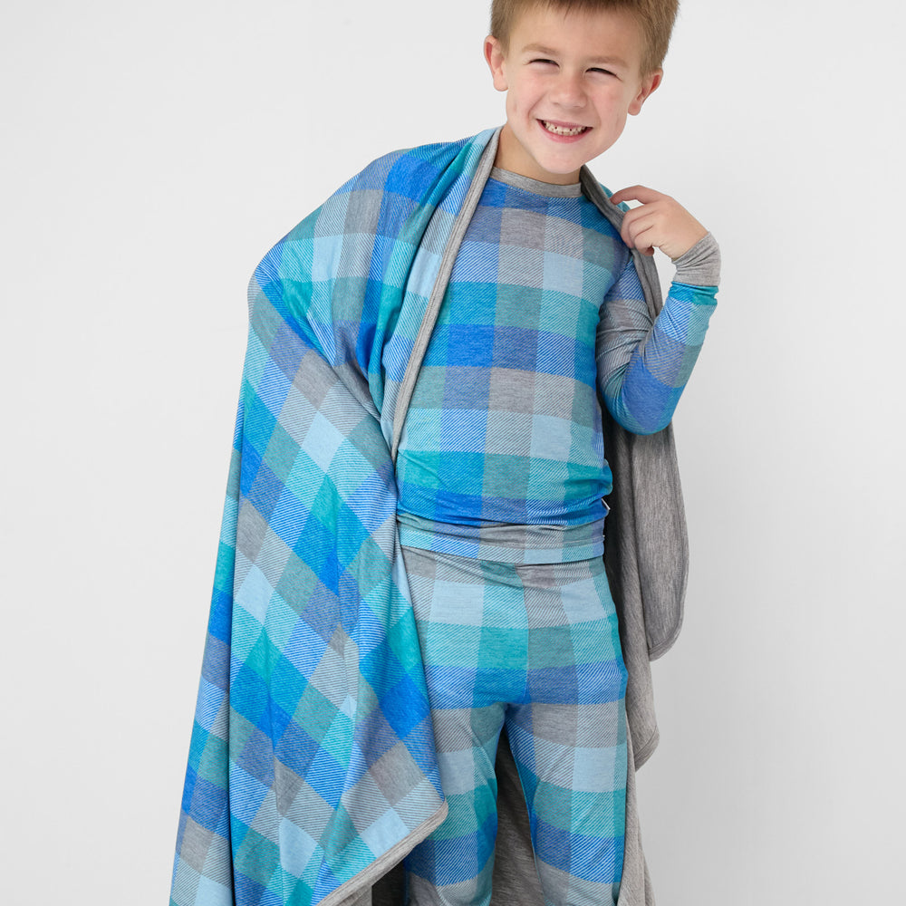 image of a child wearing an Arctic Plaid two piece pj set with a matching cloud blanket draped over his shoulders