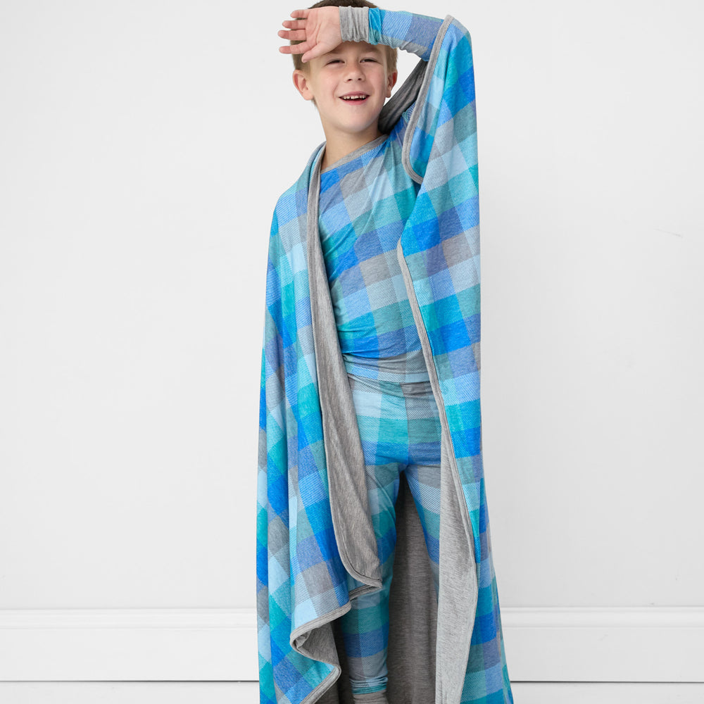 alternate image of a child posing wearing an Arctic plaid two piece pj set with a matching cloud blanket draped over his shoulders 