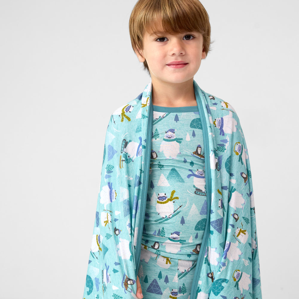 Close up image of a child wearing a Yeti Snow Day blanket over his shoulders and a matching two piece pj set