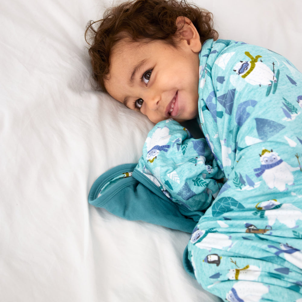 Image of a child snuggled on a bed under a Yeti Snow Day blanket