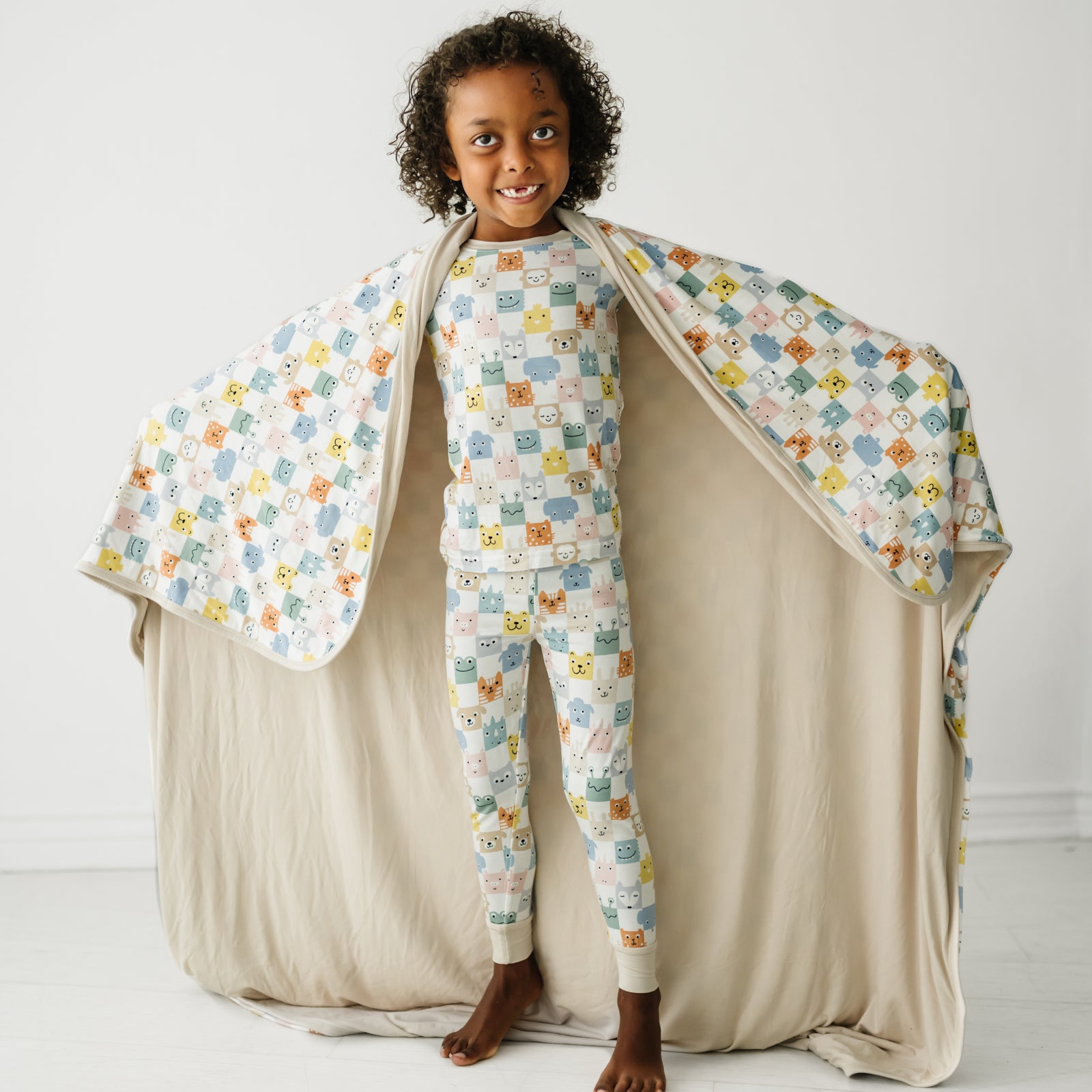 Child posing with their arms out wearing a Check Mates large cloud blanket over a matching Check mates two piece pajama set