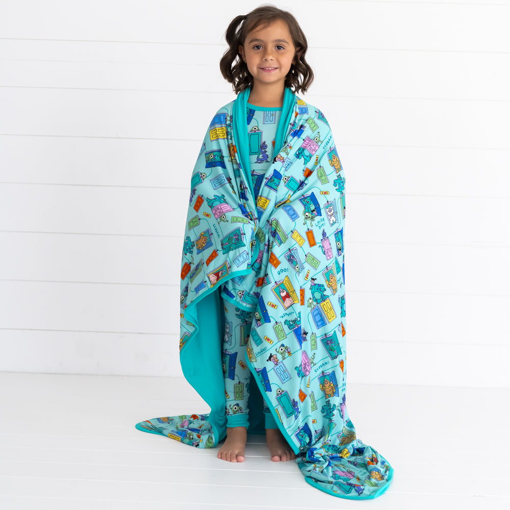 Girl wearing the Disney Monsters, Inc. Scream Team Pajama Set while wrapped in the Disney Monsters, Inc. Scream Team Large Cloud Blanket®