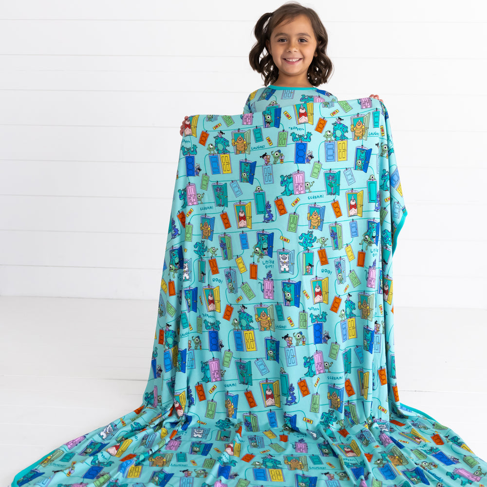 Smiling girl holding up the Disney Monsters, Inc. Scream Team Large Cloud Blanket®