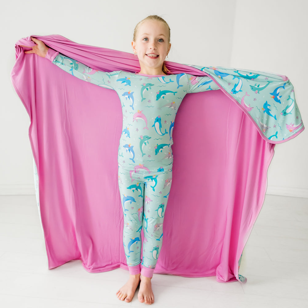 Child holding out a Dolphin Dance large cloud blanket behind them detailing the solid pink backing and wearing matching pajamas
