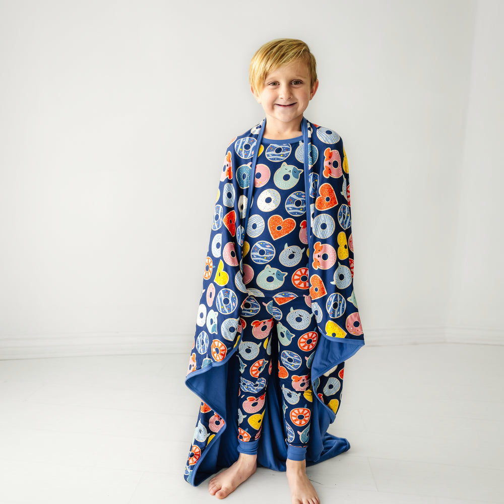 Child wearing a Blue Donut Dreams two piece pajama set with a matching large cloud blanket draped over his shoulders