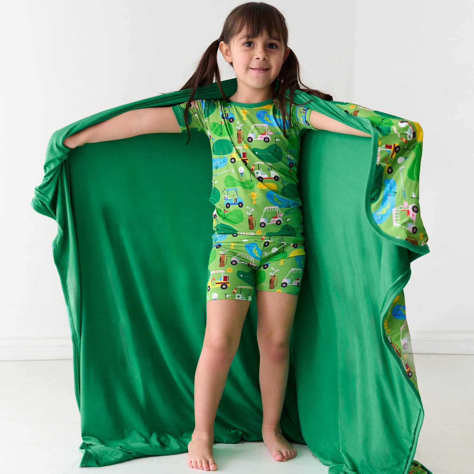 Child holding out a Fairway Fun large cloud blanket detailing the solid green backing and wearing matching pajamas