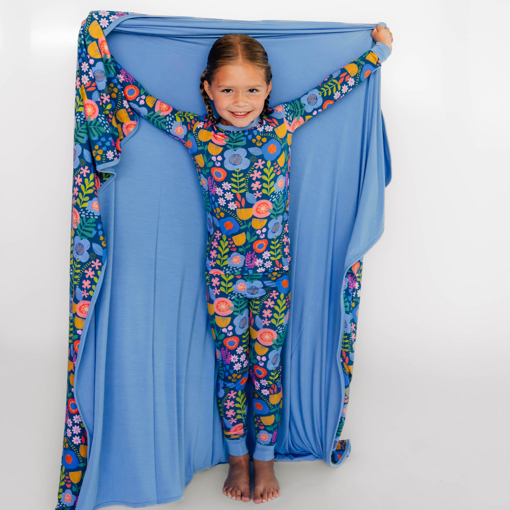 Girl holding the Folk Floral Large Cloud Blanket® to display the inside solid blue color. She is wearing the Long-sleeve Pajama Set in Folk Floral.