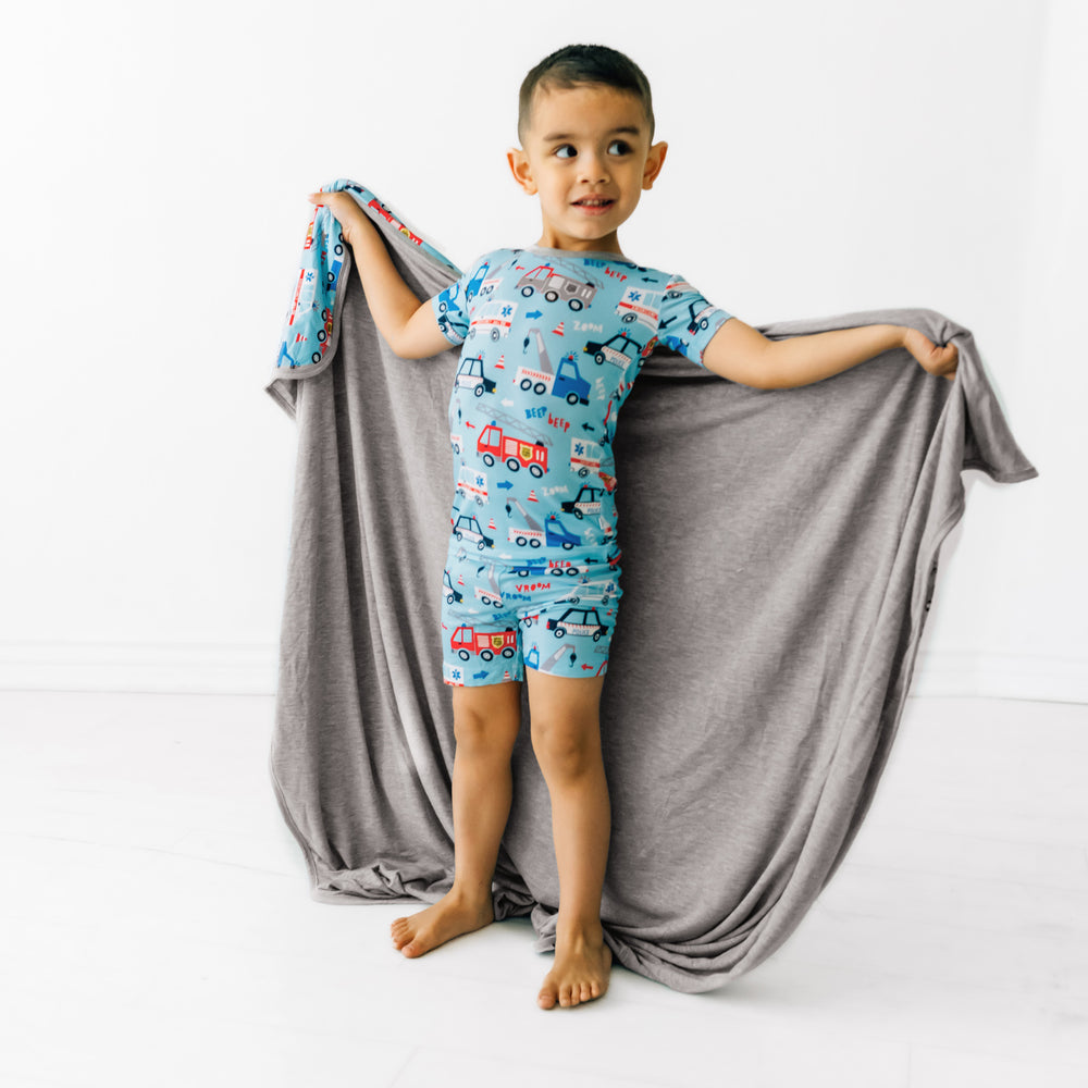 Child wearing a To The Rescue two piece short sleeve and shorts pj set. They are holding up in a To The Rescue large cloud blanket 