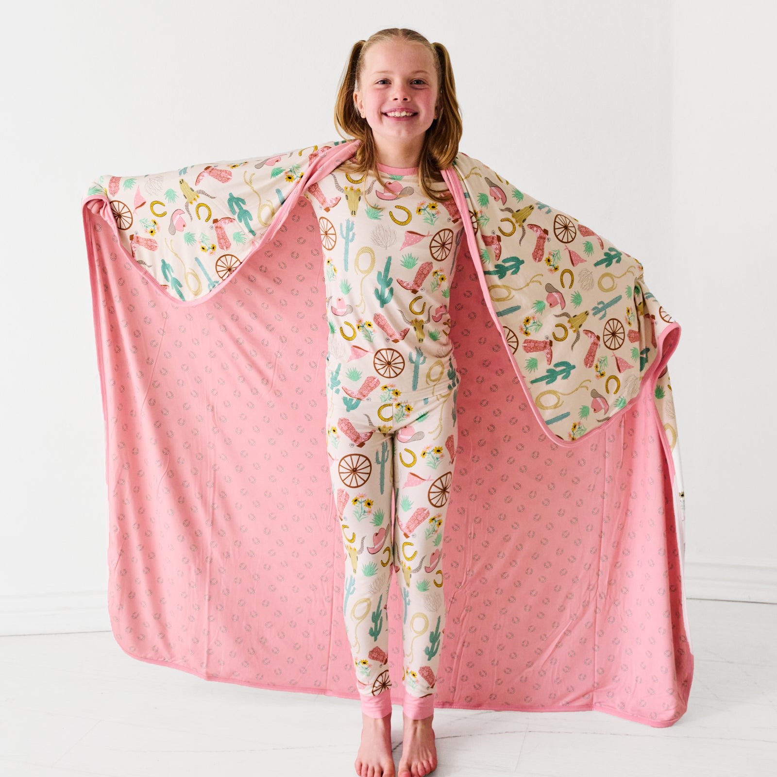 Child holding up in a Pink Ready to Rodeo large cloud blanket wearing a matching two piece pajama set