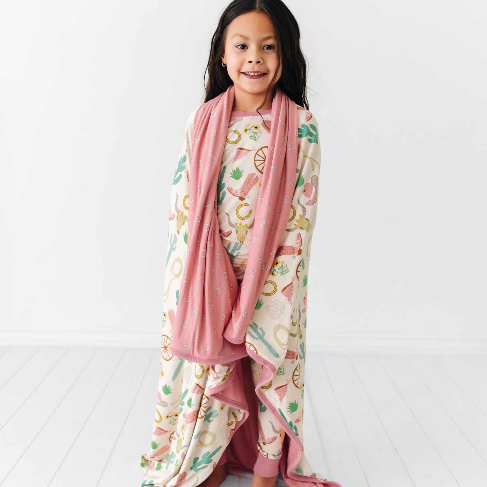Child wrapped up in a Pink Ready to Rodeo large cloud blanket wearing a matching two piece pajama set