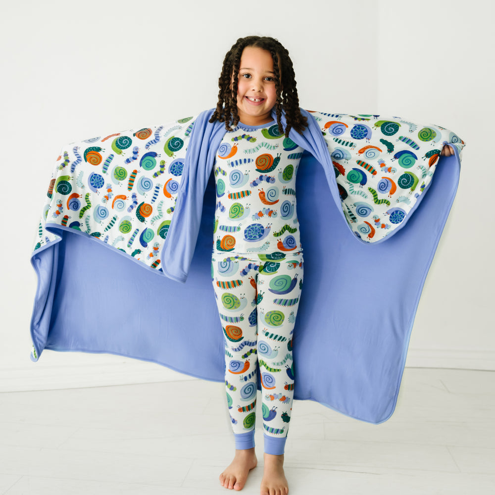 Child holding out an Inchin' Along large cloud blanket behind them, detailing the solid blue backing, and wearing matching pajamas