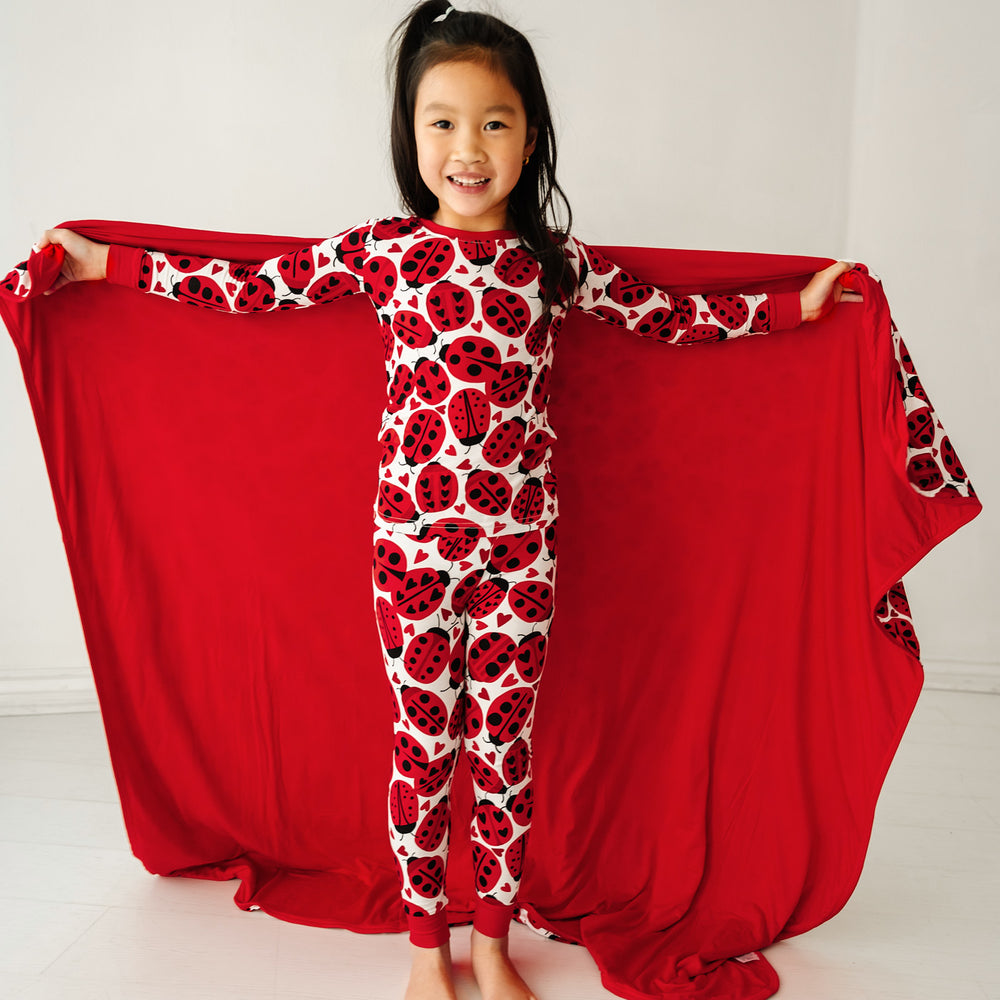 Click to see full screen - Child holding a Love Bug printed large cloud blanket behind her showing the solid red backing