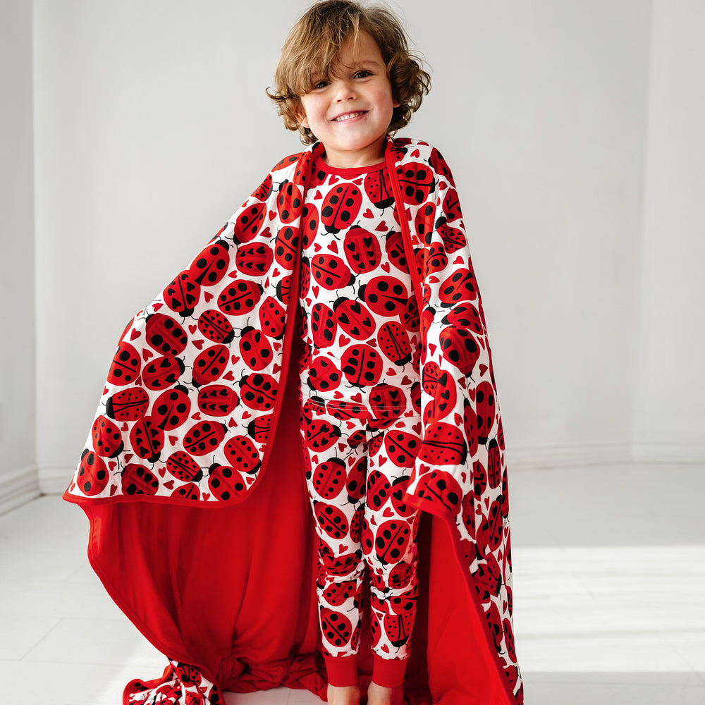 Click to see full screen - Child wrapped up in a Love Bug printed large cloud blanket showing the solid red backing