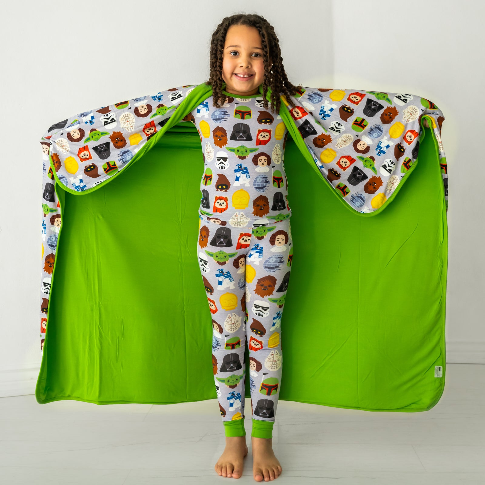 Child holding out a Legends of the Galaxy blanket behind her, detailing the solid green backing, and wearing matching pajamas