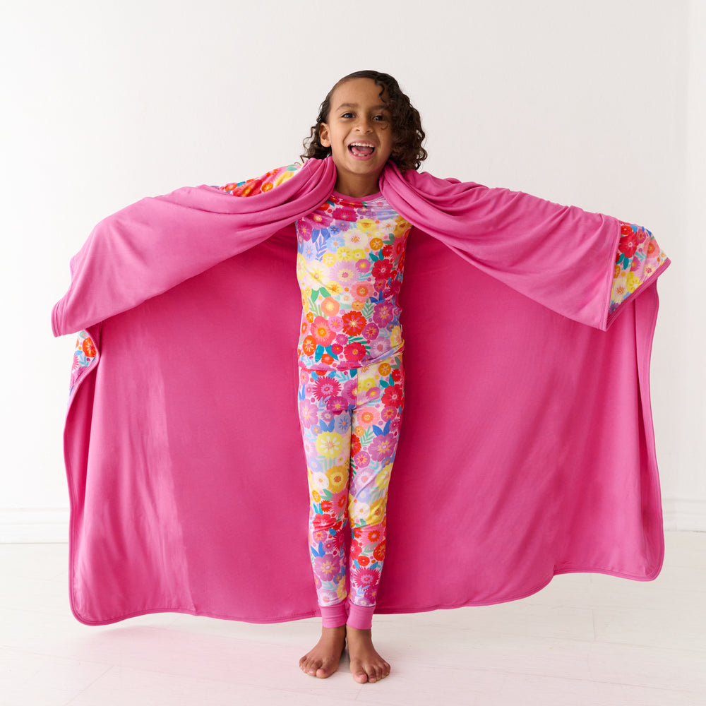 Child holding out a Rainbow Blooms large cloud blanket behind them, detailing the solid pink backing and wearing matching pajamas