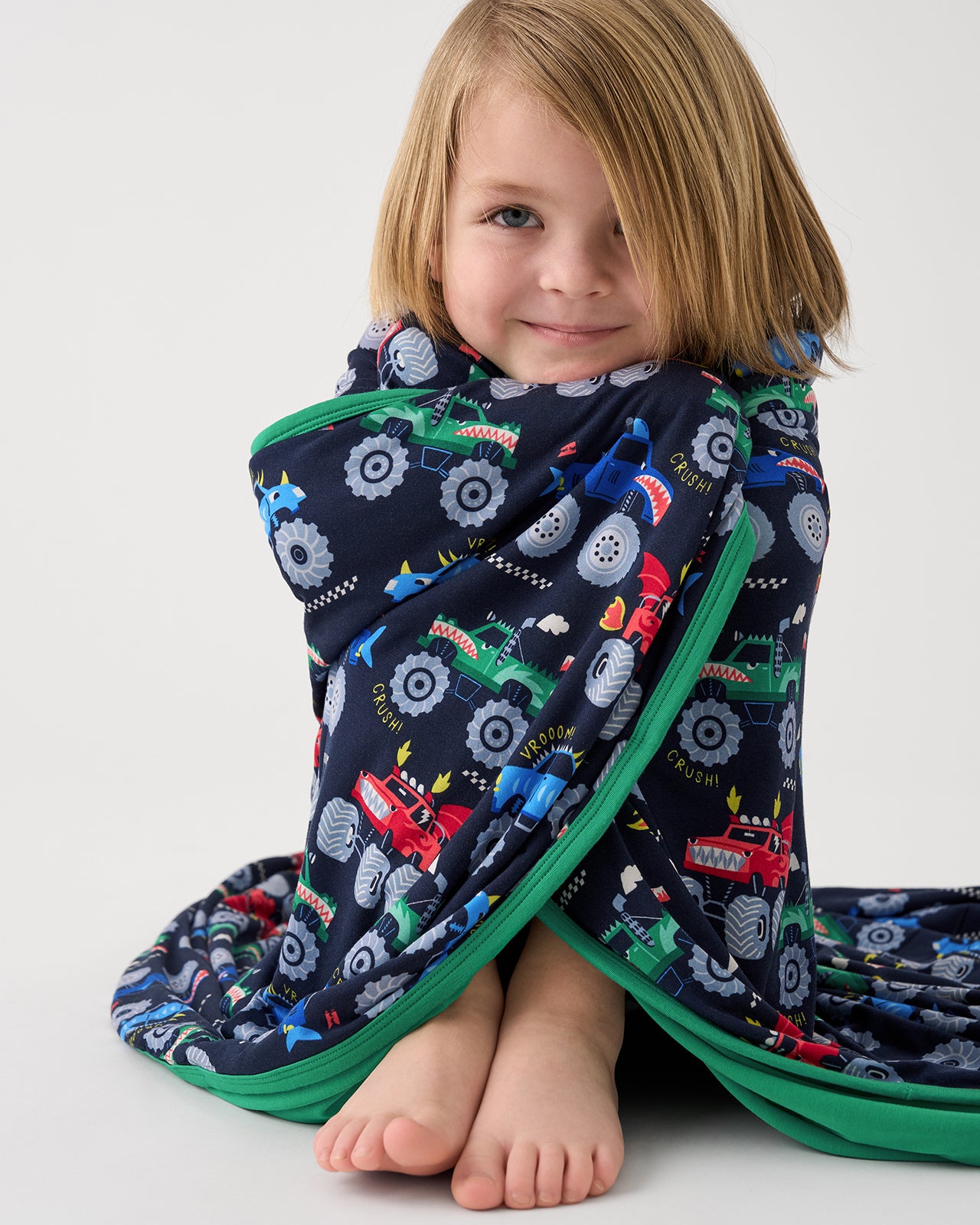 Sitting child wrapped in the Monster Truck Madness Large Cloud Blanket® 