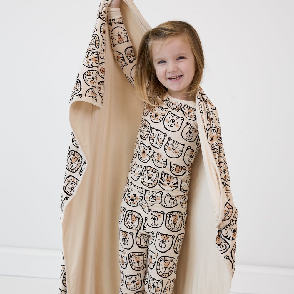 image of a child wearing a Lions, and Tigers, and Bears two piece pj set and holding up a matching cloud blanket