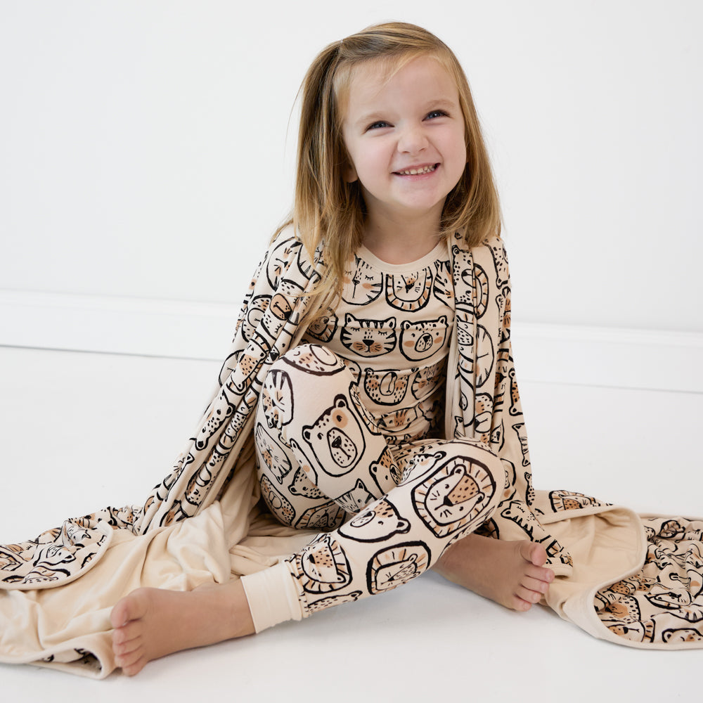 image of a child sitting wearing a Lions, and Tigers, and Bears two piece pj set and holding up a matching cloud blanket