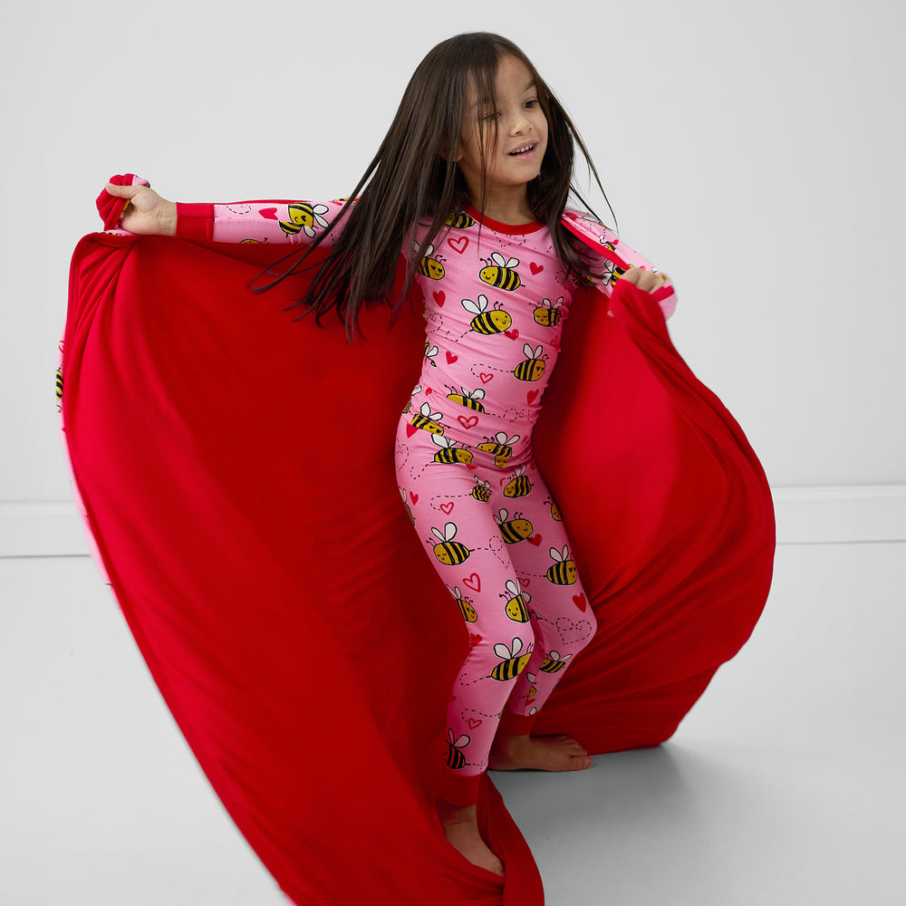 Image of a child twirling with a Pink Bee Mine blanket showing off the solid red backing and matching two piece pj set