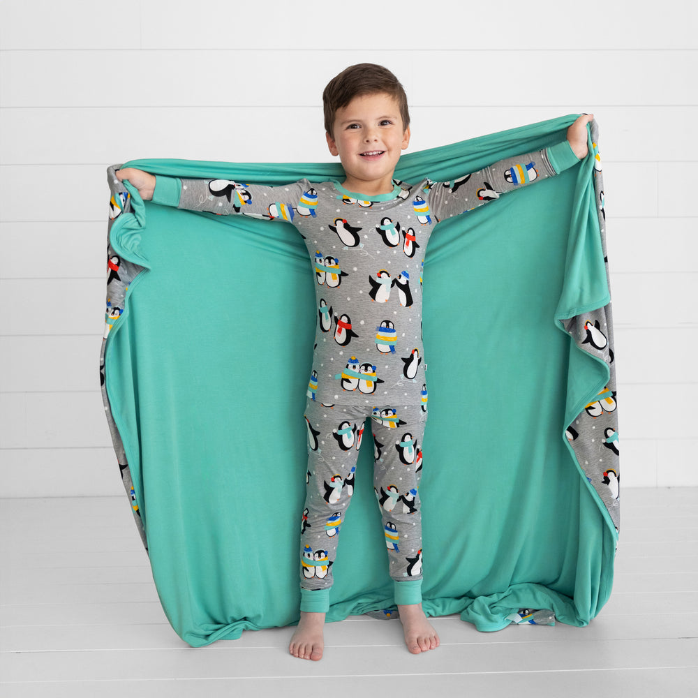 child holding out a Penguin Party blanket over his shoulders and matching two piece pj set