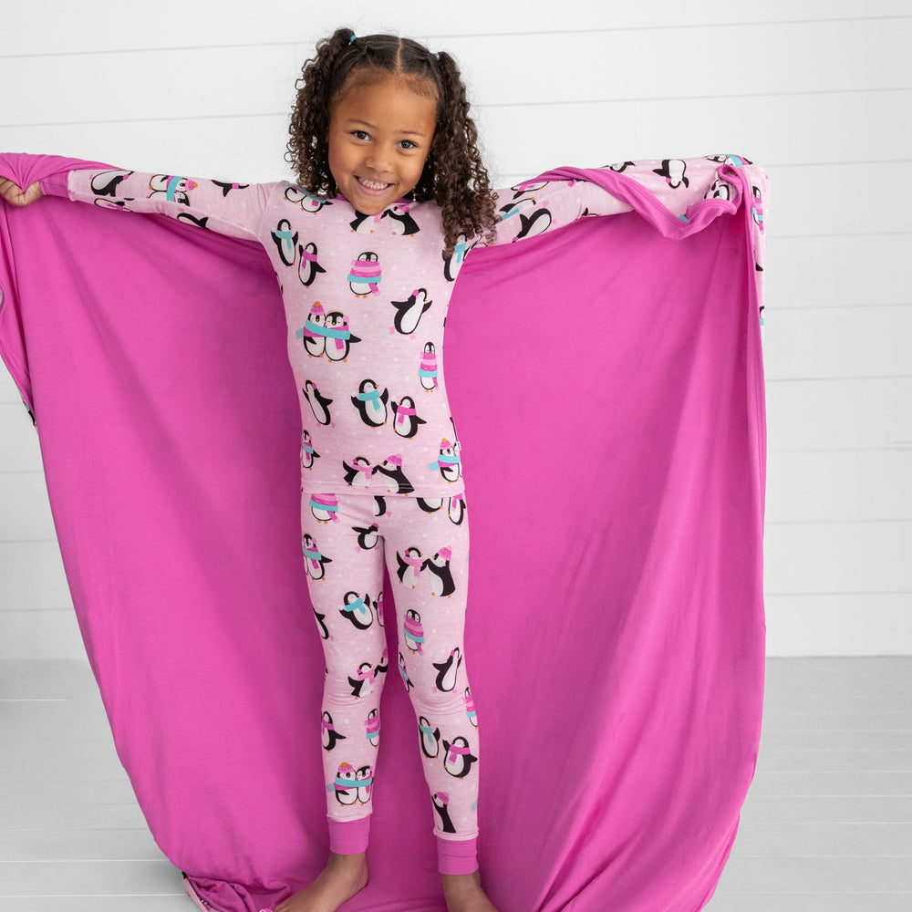 Child holding out a Pink Penguin Party blanket and wearing matching two piece pj set