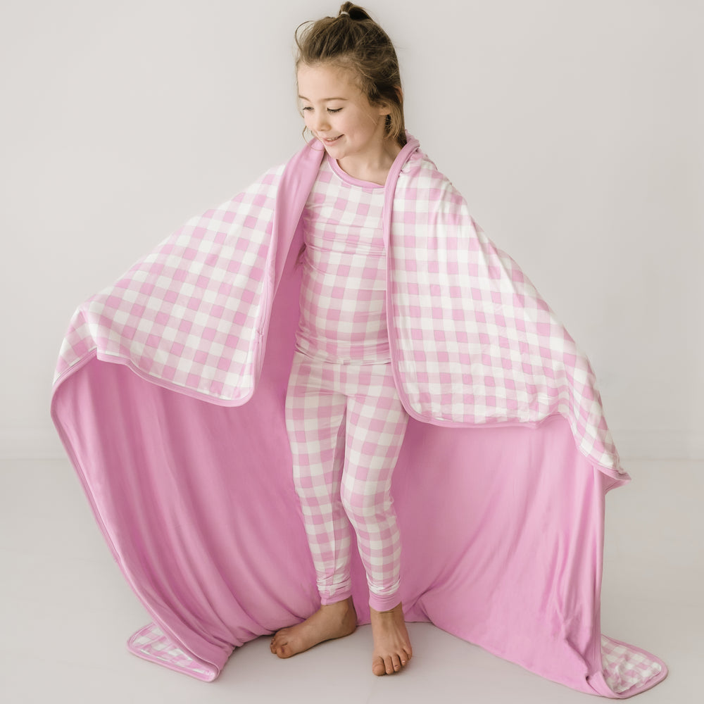 Click to see full screen - Child wearing a Pink Gingham cloud blanket over her shoulders and a matching pink gingham two piece pajama set