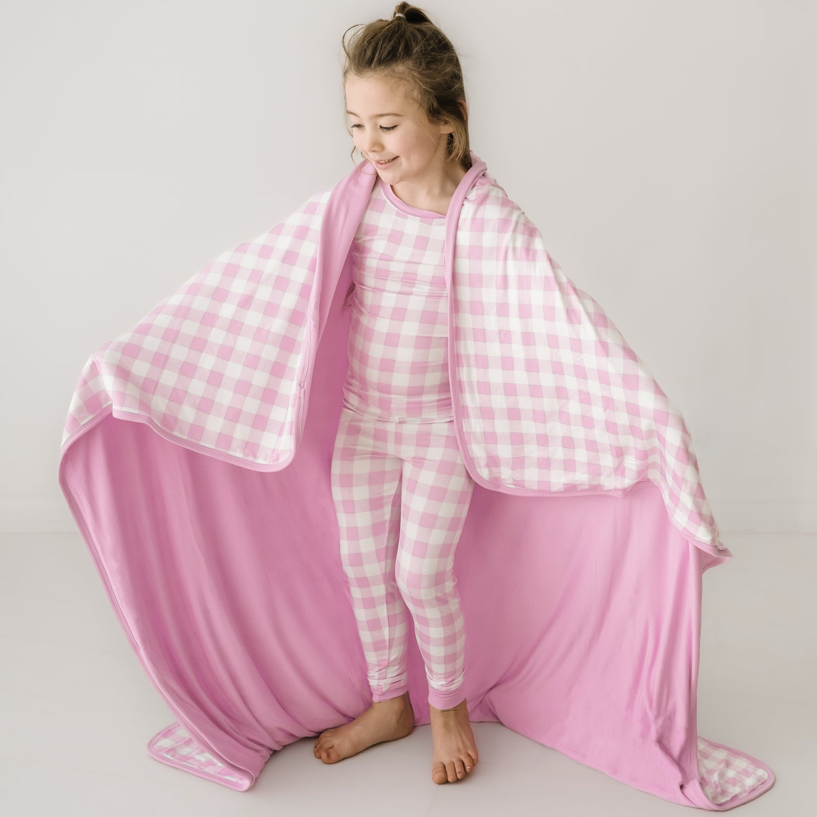 Child wearing a Pink Gingham cloud blanket over her shoulders and a matching pink gingham two piece pajama set