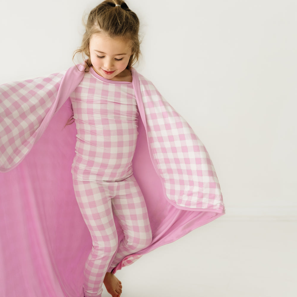 Click to see full screen - Alternate close up image of a child wearing a Pink Gingham cloud blanket over her shoulders and a matching pink gingham two piece pajama set