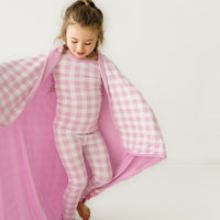Alternate close up image of a child wearing a Pink Gingham cloud blanket over her shoulders and a matching pink gingham two piece pajama set