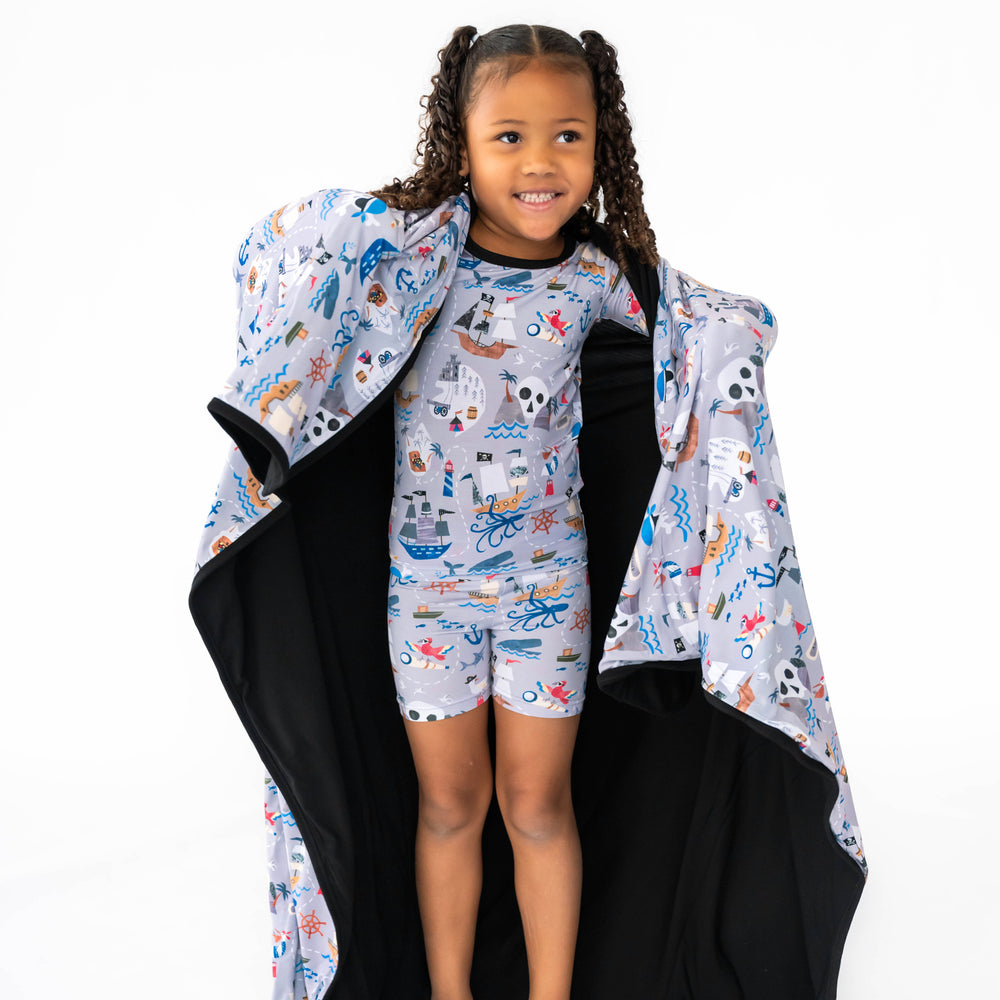 Girl standing while wearing the Pirate's Map Short-sleeve Shorts Pajama Set and showing the inside of the Pirate's Map Large Cloud Blanket® 