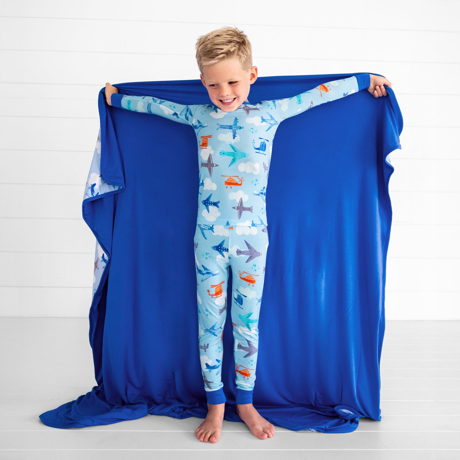 child wearing two piece lets fly pjs holding out a matching cloud blanket showing the blue backing