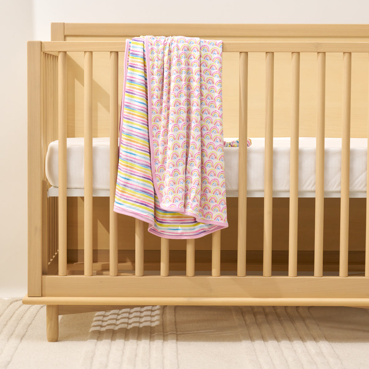 pastel rainbow blanket with striped background laying over crib