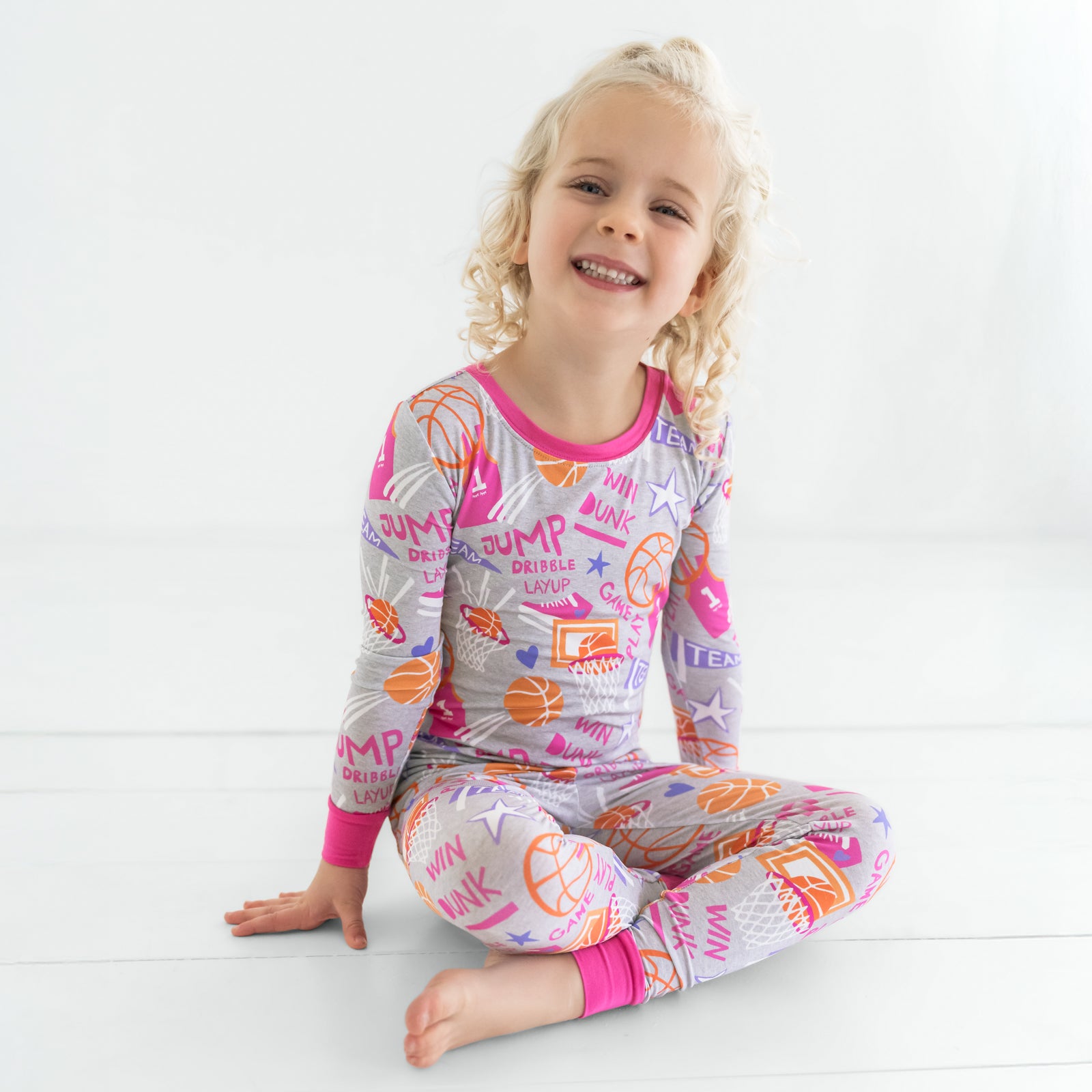 Child sitting wearing the Pink Slam Dunk bamboo kids pajamas