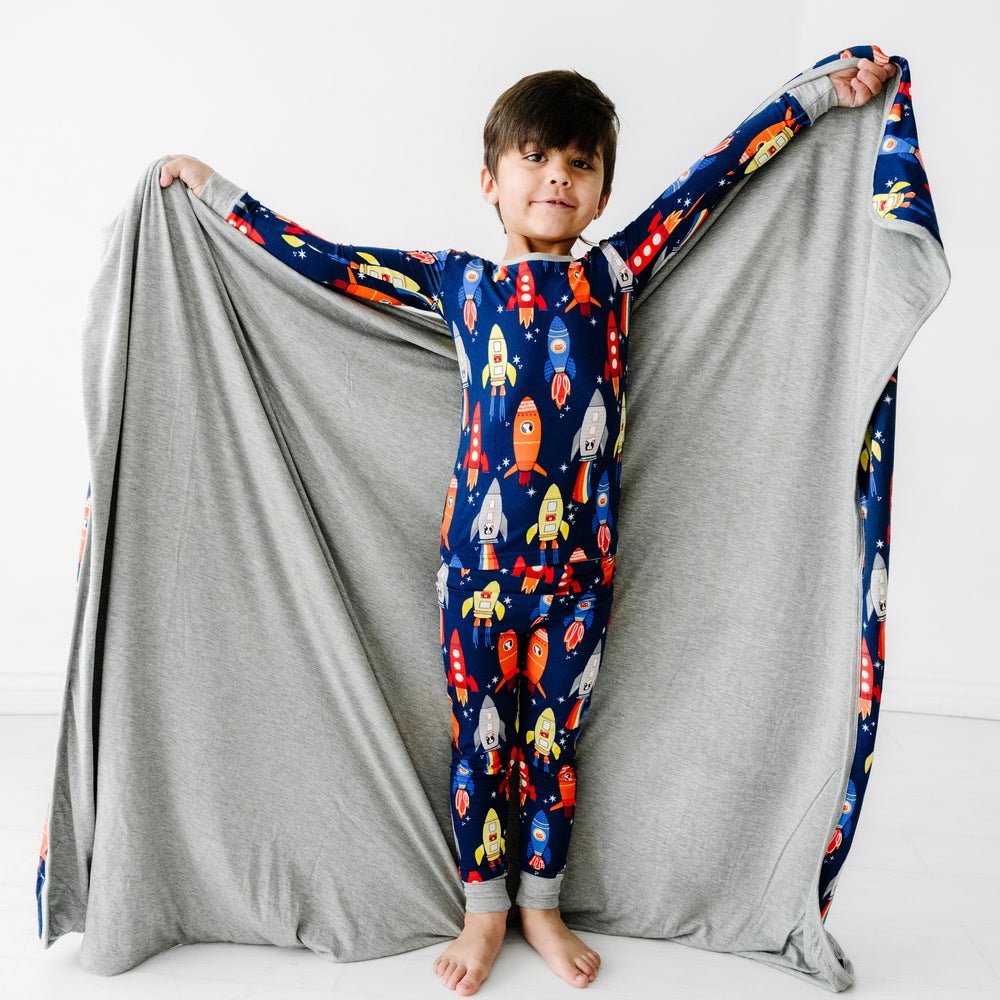 child holding up a Navy space explorer cloud blanket wearing a matching printed two piece pajama set