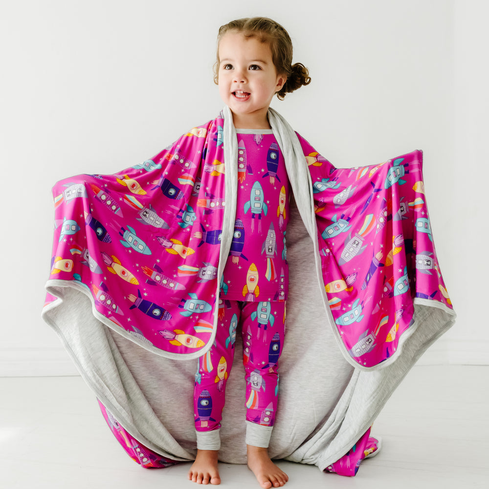 Child wearing a Pink Space Explorers blanket over her shoulders and a matching two piece pajama set