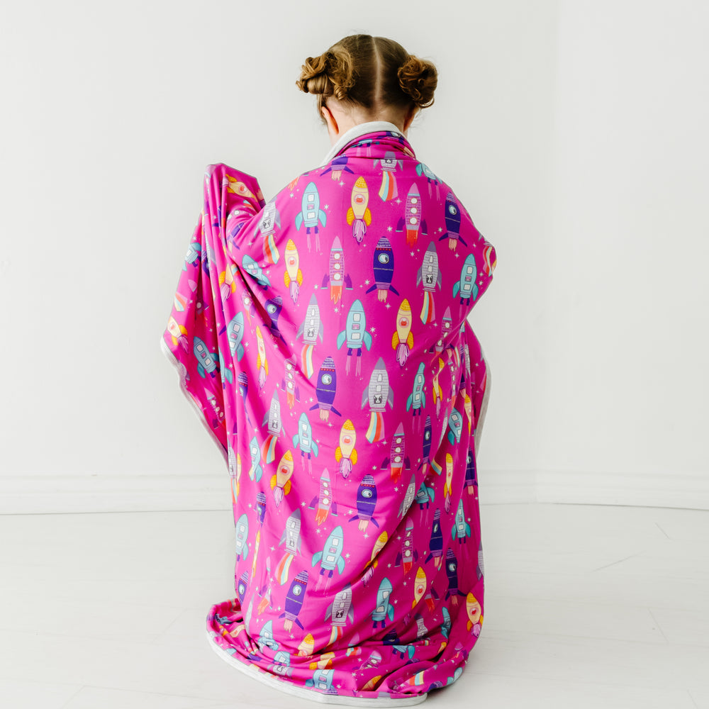 Back view of a child wearing a Pink Space Explorer cloud blanket over her shoulders
